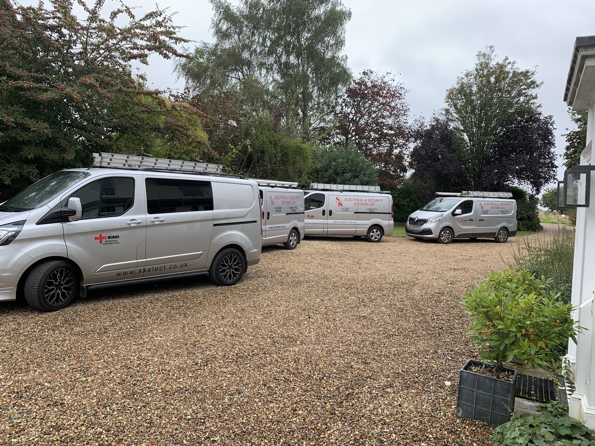 Four silver SK Electrical vans with red livery and ladders on the roof racks