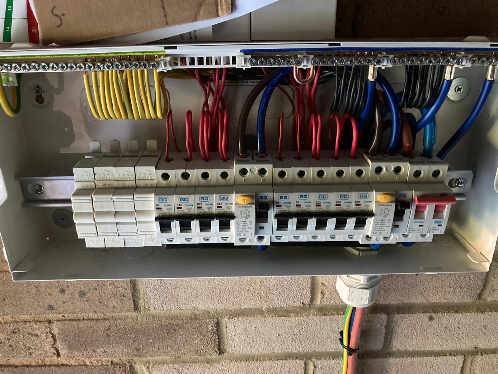 A metal consumer unit on a brick wall, cover off, with neat red, black and blue wiring